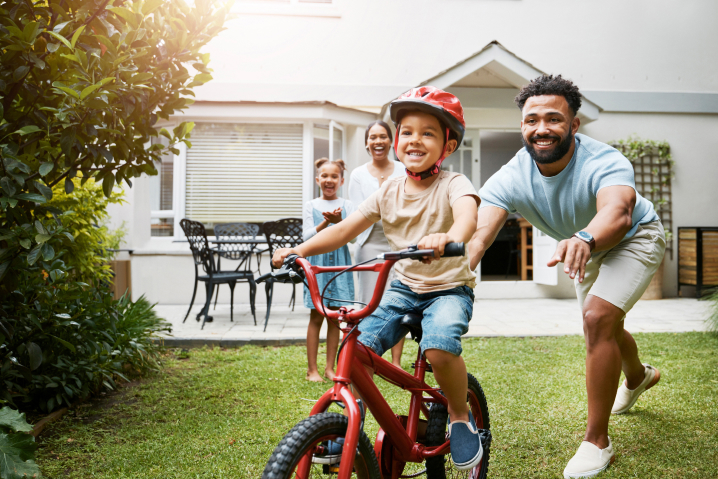 Dad pushing son on bike with mom and sister watching