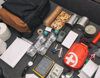 Emergency gear laid out on table with water, scissors, flashlight, cash, dry goods, toilet paper