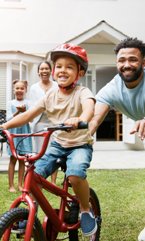 Dad pushing son on bike with mom and sister watching