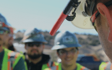 Upclose side image of male face with hardhat and three blurred people behind him