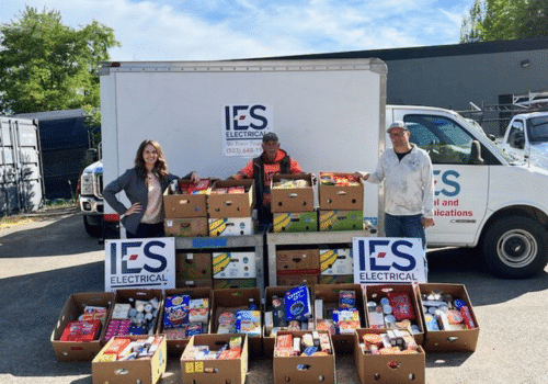 Three IES employees standing in front of foodbank donation