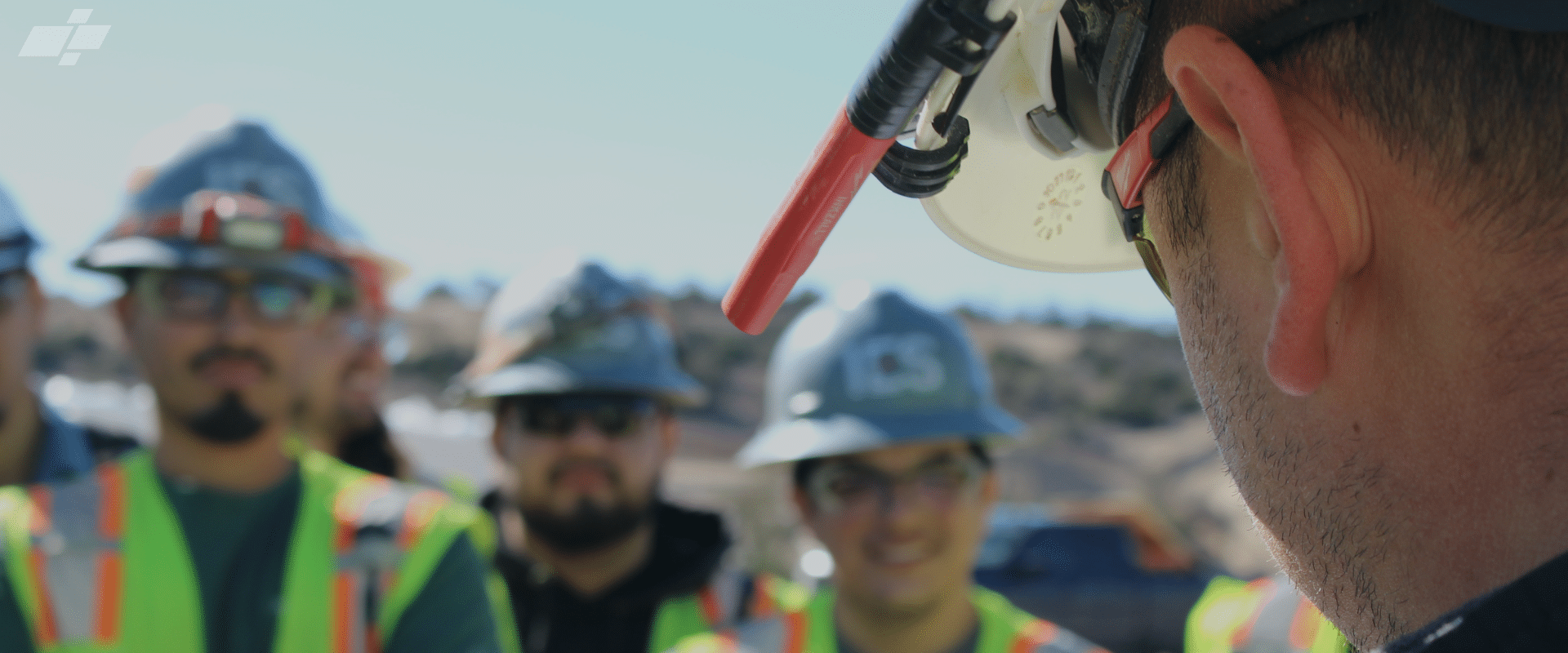 Upclose side image of male face with hardhat and three blurred people behind him