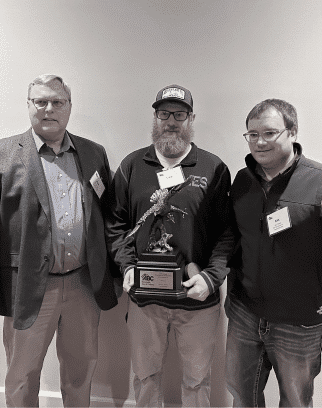 Black and white image of three IES employees with the middle person holding an eagle award