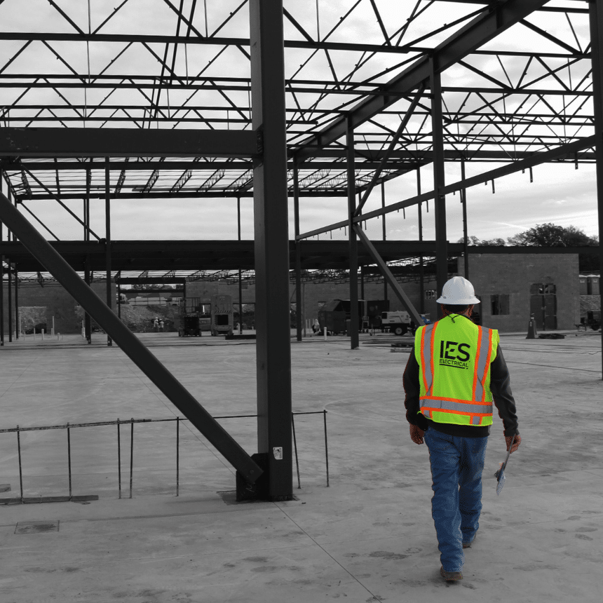 Man in safety vest and white hardhat walking through steel framed building