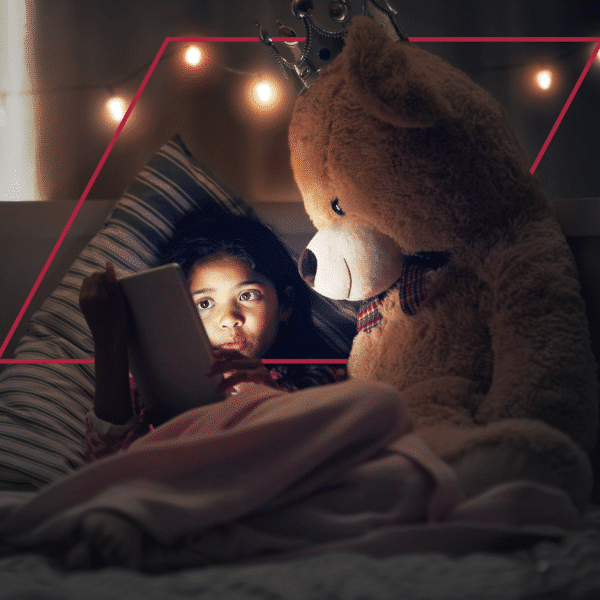 Little girl playing with tablet beside big teddy bear