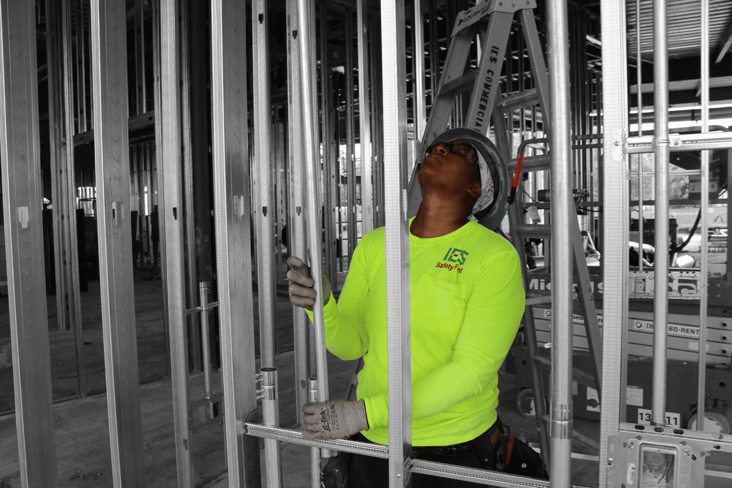 woman in hardhat and safety glasses looking up a beam