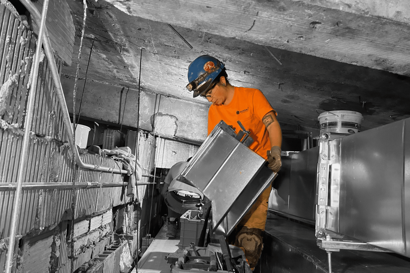 Woman in orange shirt and blue hardhat attaching HVAC components