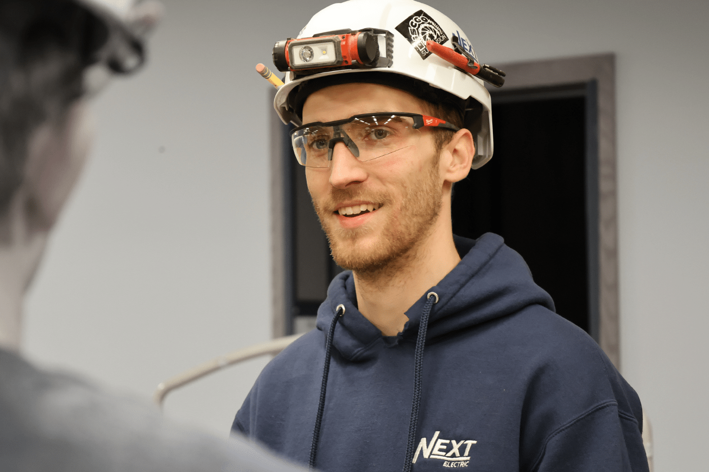 Man in white hardhat and blue sweatshirt smiling at person off camera