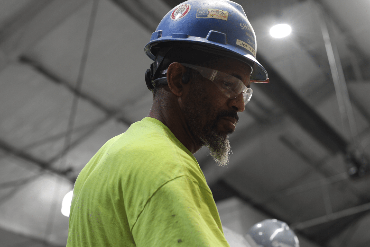 Man in yellow safety tshirt and blue hardhat and safety glasses looking down