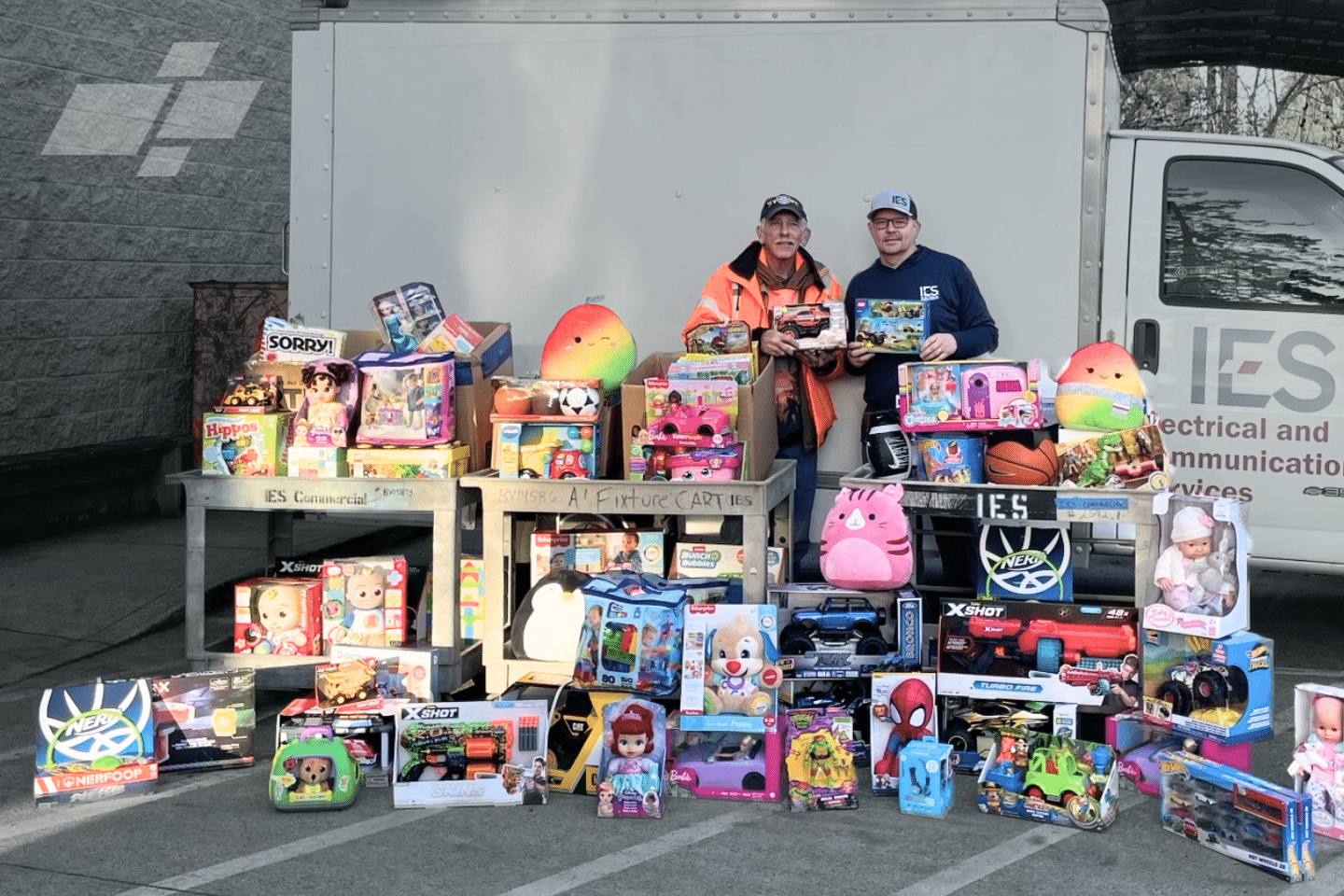 Two IES employess standing behind a mountain of toys in front of an IES truck